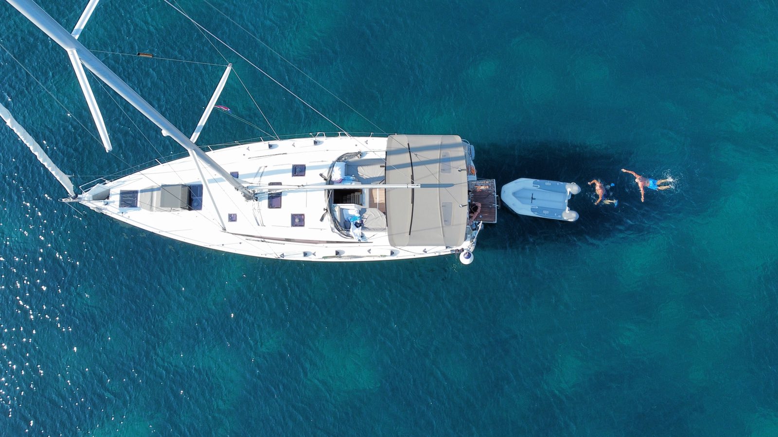 A yacht at anchor with the dinghy astern and swimmers in the water